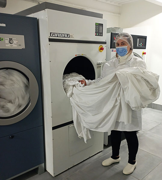 Photo dans notre atelier de blanchisserie de Palaiseau d'une de nos blanchisseuses sortant du linge d'un lave-linge industriel