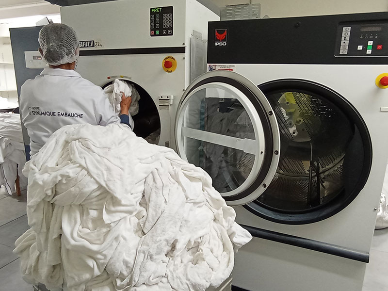 Photo dans notre atelier de blanchisserie de Palaiseau d'une de nos blanchisseuses chargeant du linge dans un lave-linge industriel